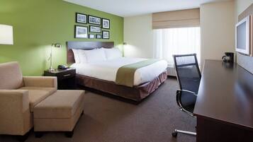 Habitación de hotel con cama, escritorio, silla, lámpara, mesita de noche y cuadros en la pared.