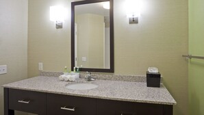 A bathroom with a granite countertop, a white sink, a dark vanity with drawers, a large mirror, and two wall-mounted lights. - Holiday Inn Express Hotel & Suites Rogers by IHG (Rogers)