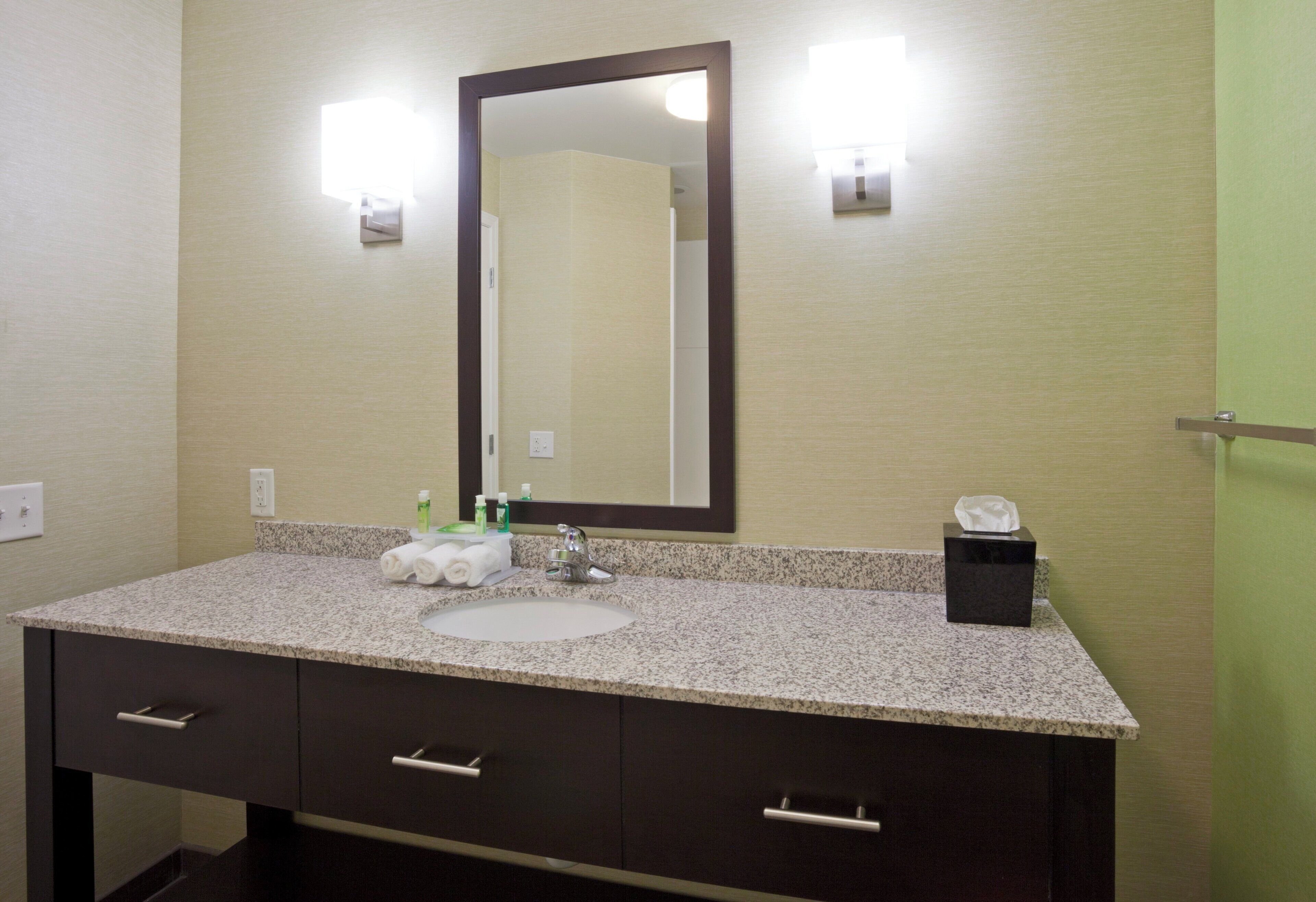 A bathroom with a granite countertop, a white sink, a mirror, and a tissue box.