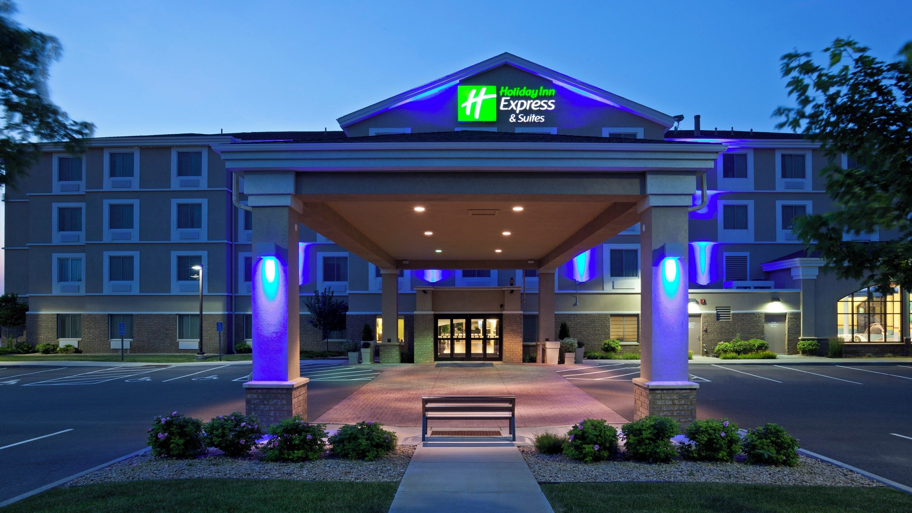 A Holiday Inn Express & Suites hotel entrance with a covered walkway, a bench, and a well-lit facade.