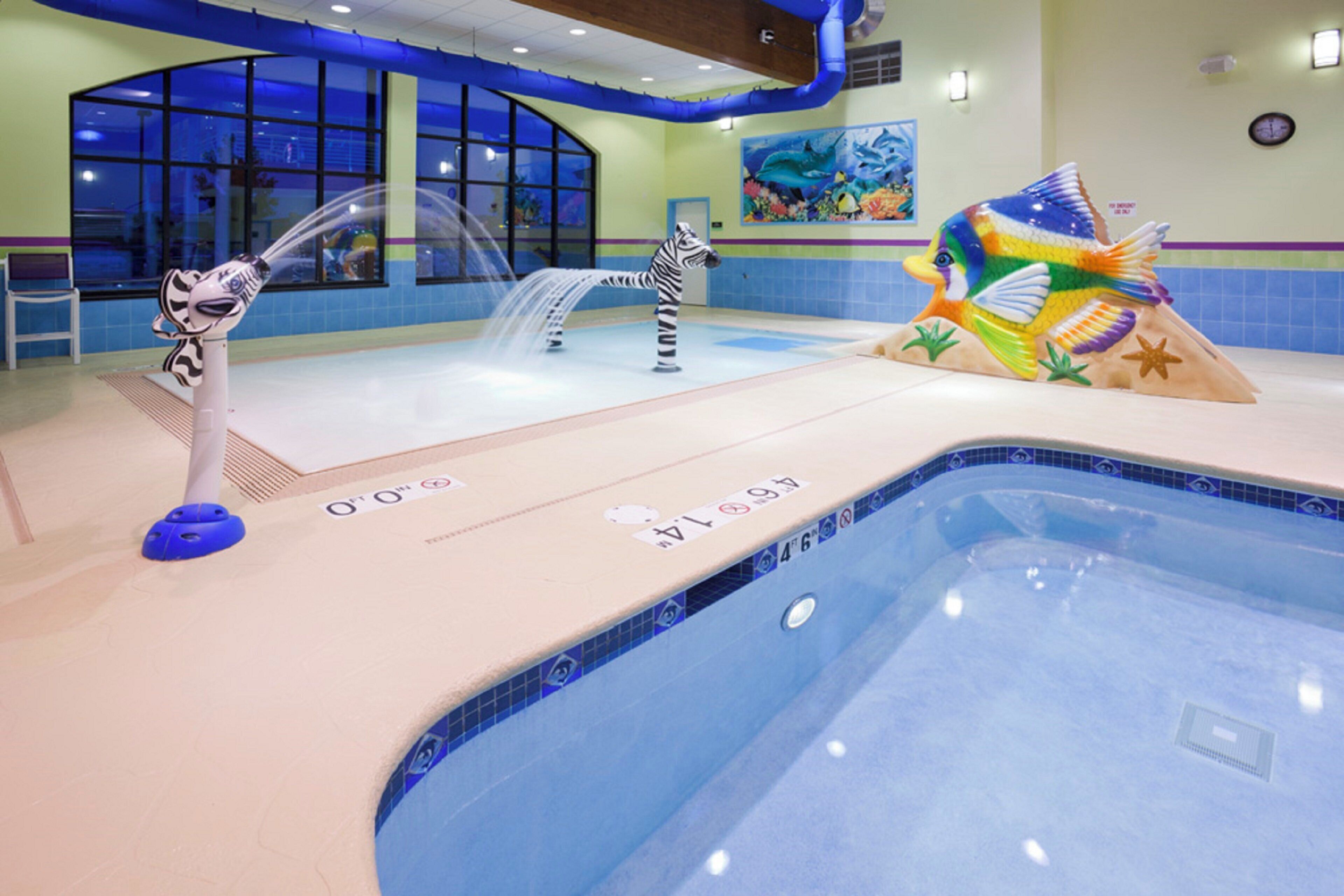 An indoor swimming pool with a zebra statue, a dolphin statue, and a colorful fish statue.