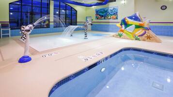 An indoor swimming pool with a zebra statue, a dolphin statue, and a colorful fish statue.