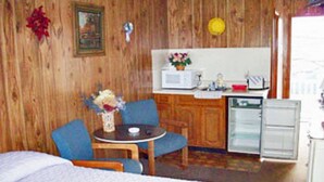 A room with a bed, a small table with a vase of flowers, a blue chair, a kitchenette with a microwave, and a refrigerator. - Moby Dick Motel (Old Orchard Beach)