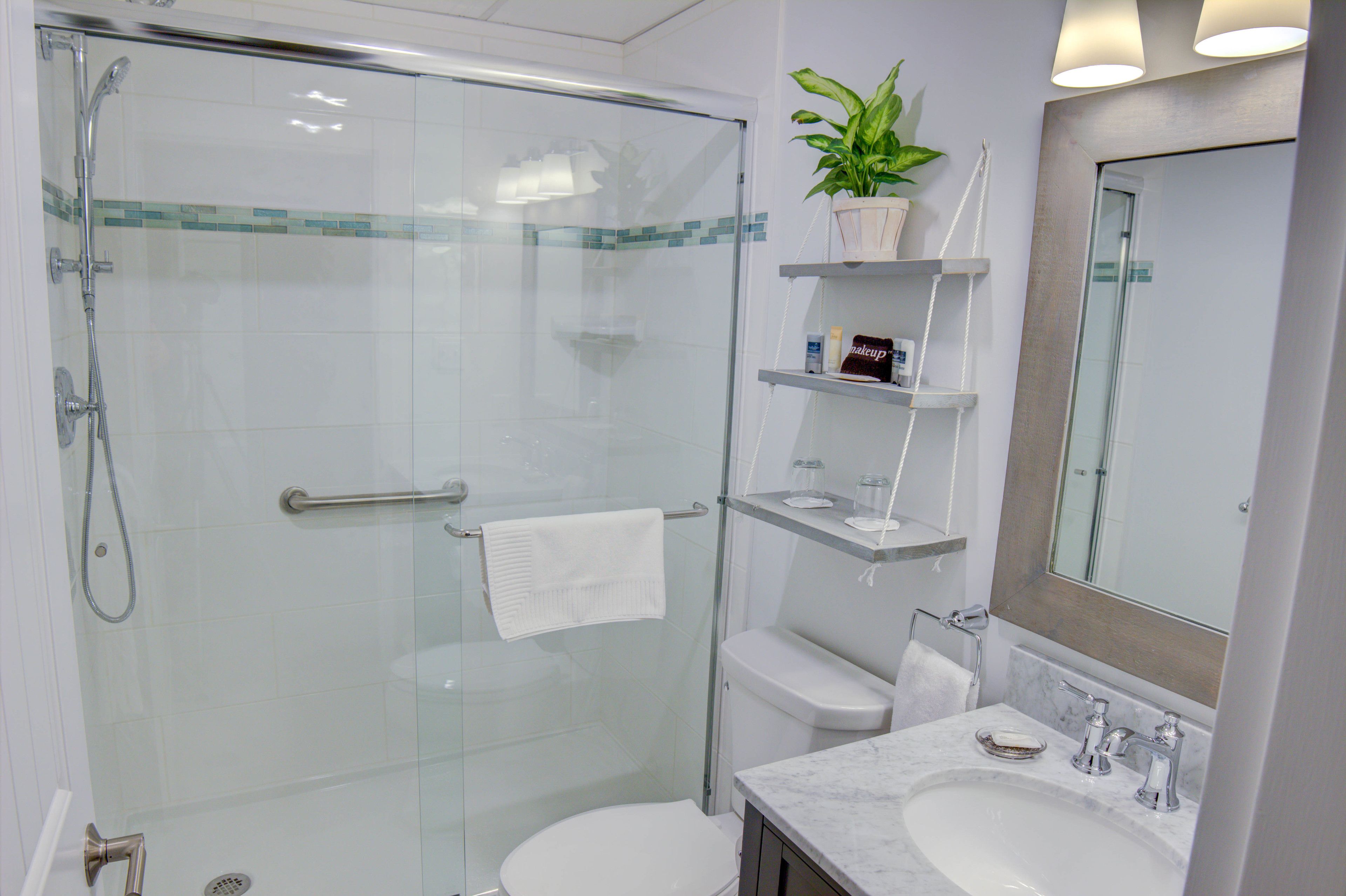 Ein modernes Badezimmer mit einer Glaskabine zur Dusche, einer Toilette, einem Waschbecken mit Marmorplatte und einem Spiegel darüber.