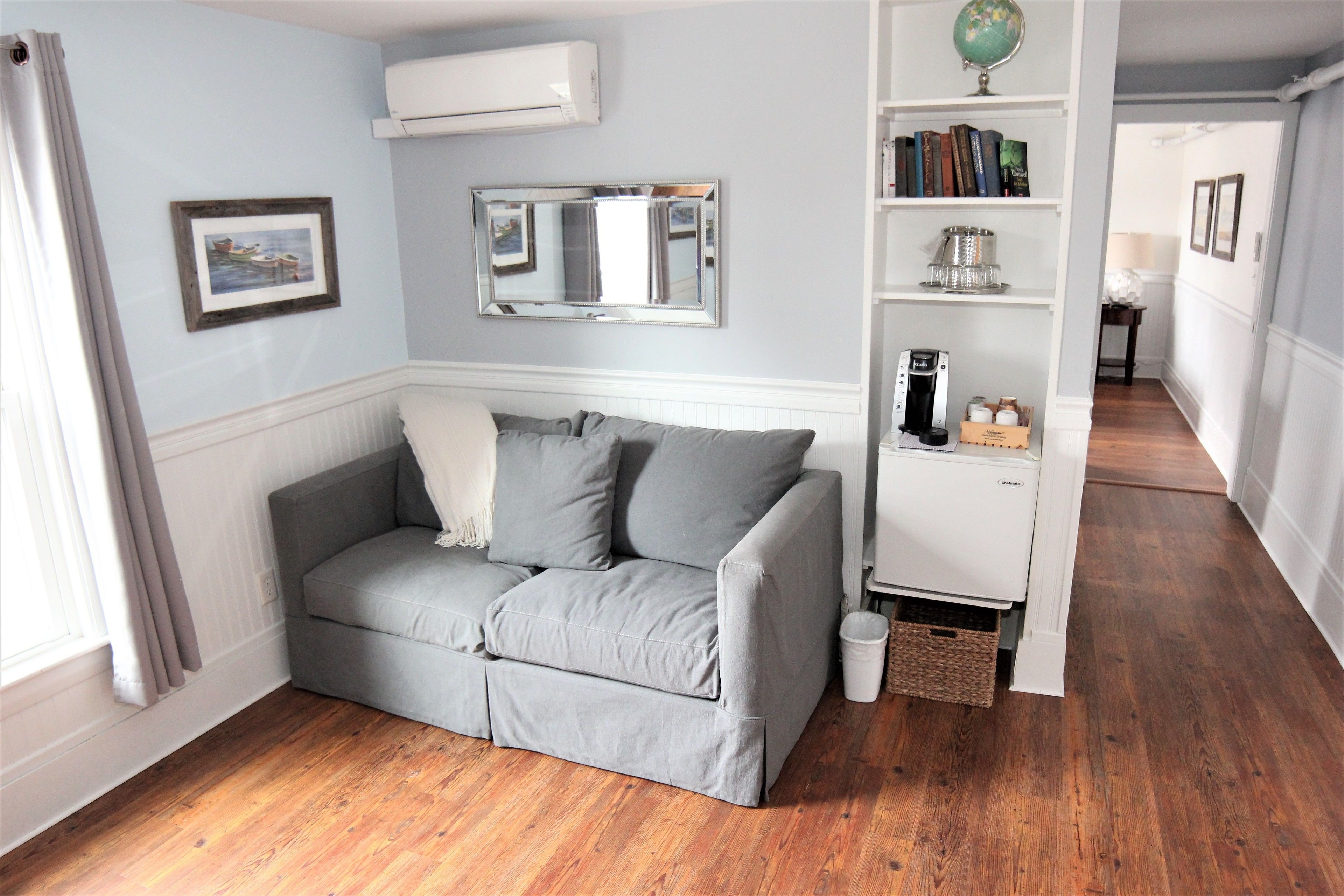 Ein Zimmer mit grauem Sofa, einem Bücherregal, einem Globus und einer Heizung.