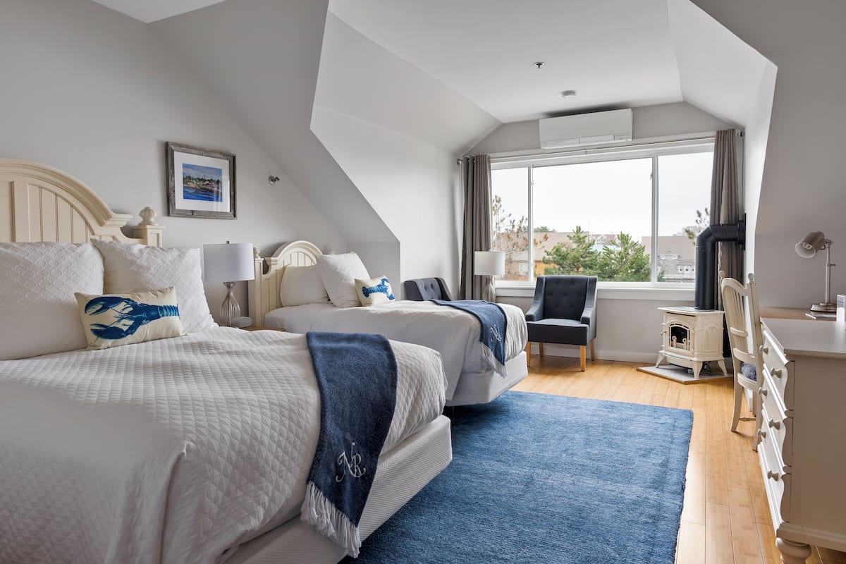 Ett sovrum med två sängar, ett stort fönster och utsikt över staden.