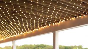 An outdoor dining area with wooden tables and chairs, string lights overhead, and a view of greenery in the background. - Nonantum Resort (Kennebunkport)
