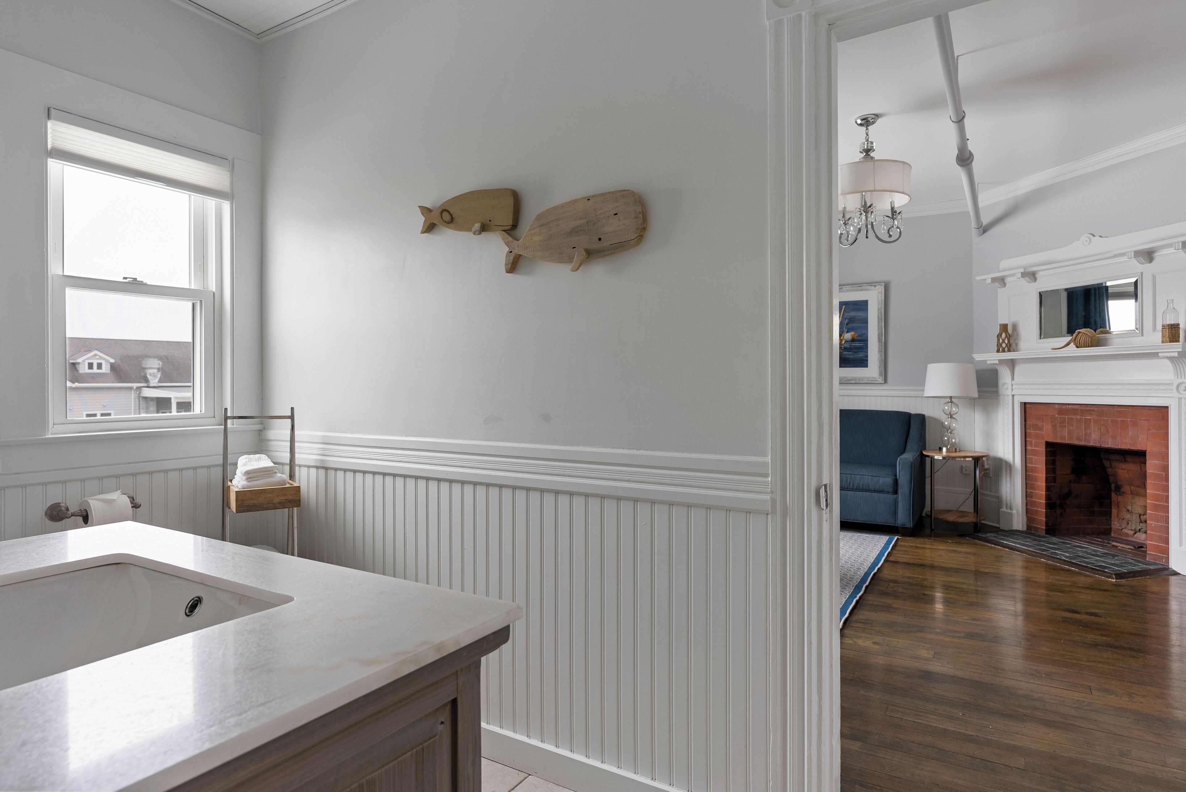 Une salle de bain avec un grand lavabo, des éléments de décoration murale en bois, un porte-serviettes et une fenêtre avec des stores.