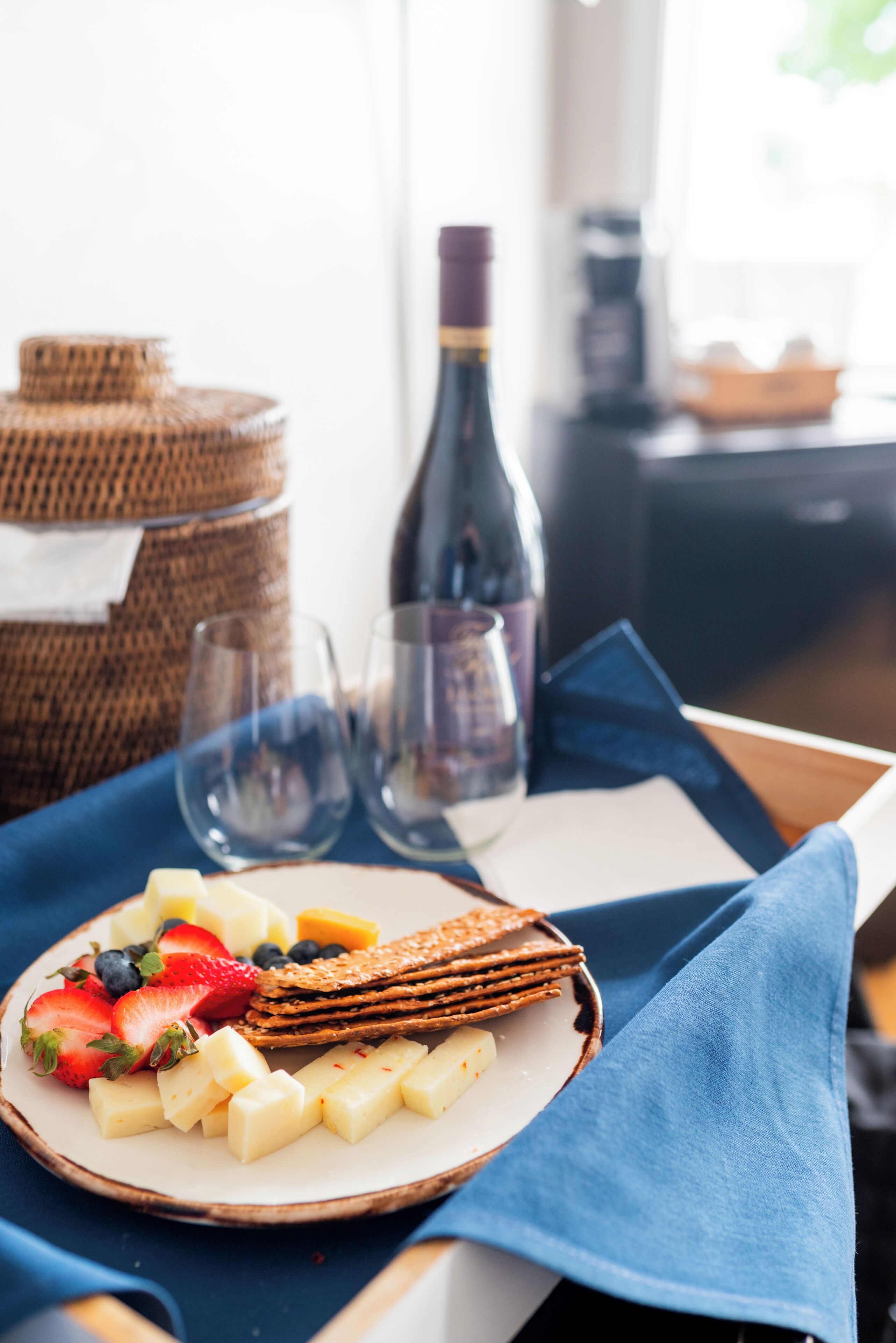 Une assiette de fromage, de crackers et de fruits est posée sur une table, avec une serviette bleue à côté.