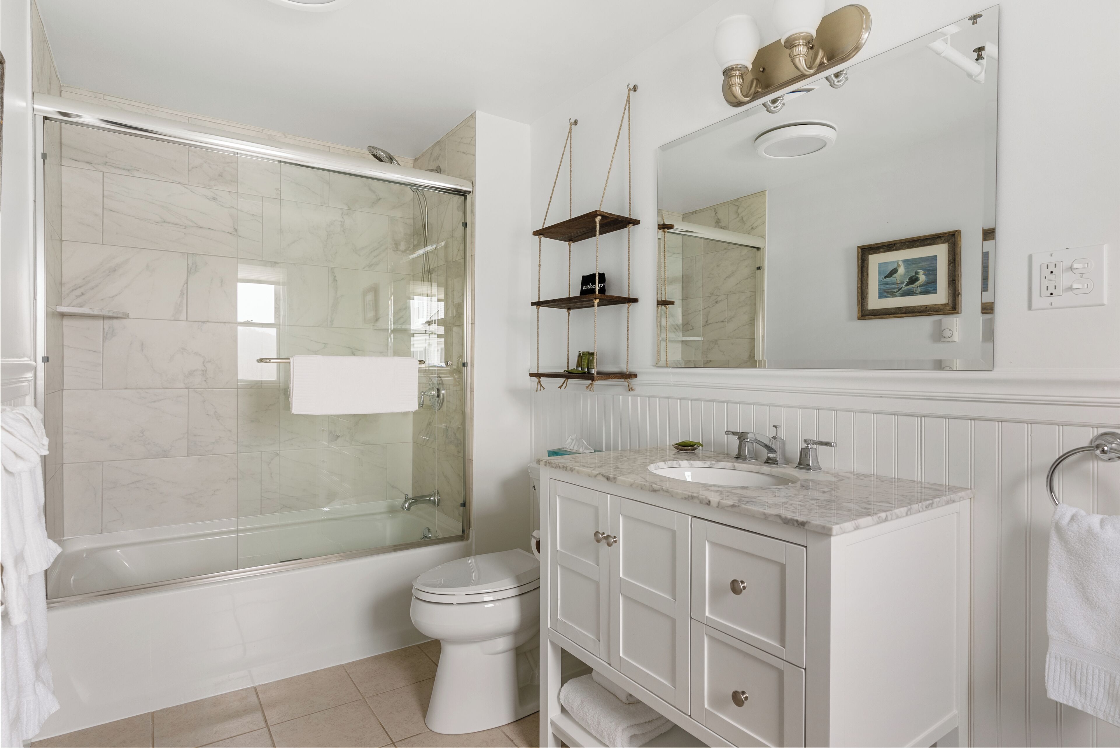 A bathroom with a glass-enclosed shower, a white toilet, a sink with a marble countertop, and a vanity with cabinets.