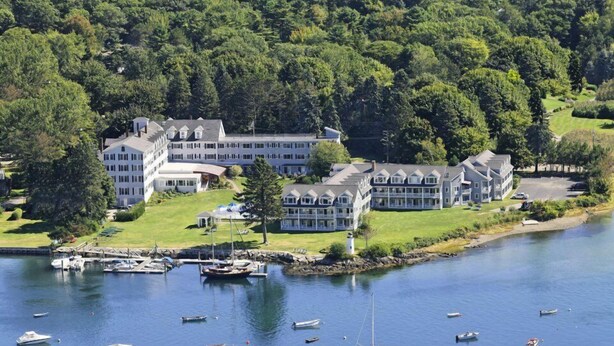 A large, multi-story hotel with a waterfront view, docked boats, and lush greenery. - Nonantum Resort (Kennebunkport)