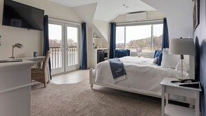 A bedroom with a large bed, a desk, a TV, and a balcony with curtains. - Nonantum Resort (Kennebunkport)