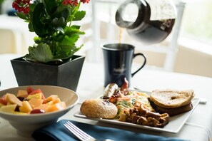 A breakfast setting with a bowl of fruit, a plate of eggs, toast, and a coffee pot.