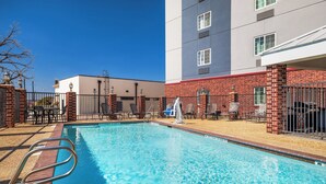 A swimming pool with a metal ladder, surrounded by a brick wall and a building with multiple windows. - Candlewood Suites San Antonio NW Near Seaworld by IHG (San Antonio)