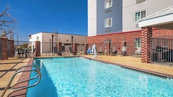 A swimming pool with a metal ladder, surrounded by a brick wall and a building with multiple windows.