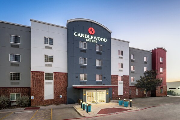 Un hotel de varios pisos con un llamativo letrero de 'Candlewood Suites', fachada de ladrillo y un estacionamiento.