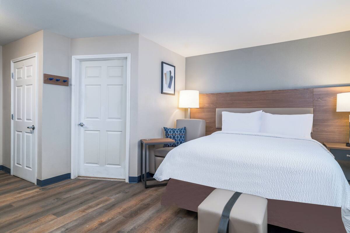 A hotel room with a bed, bedside tables, a lamp, a chair, and a door.