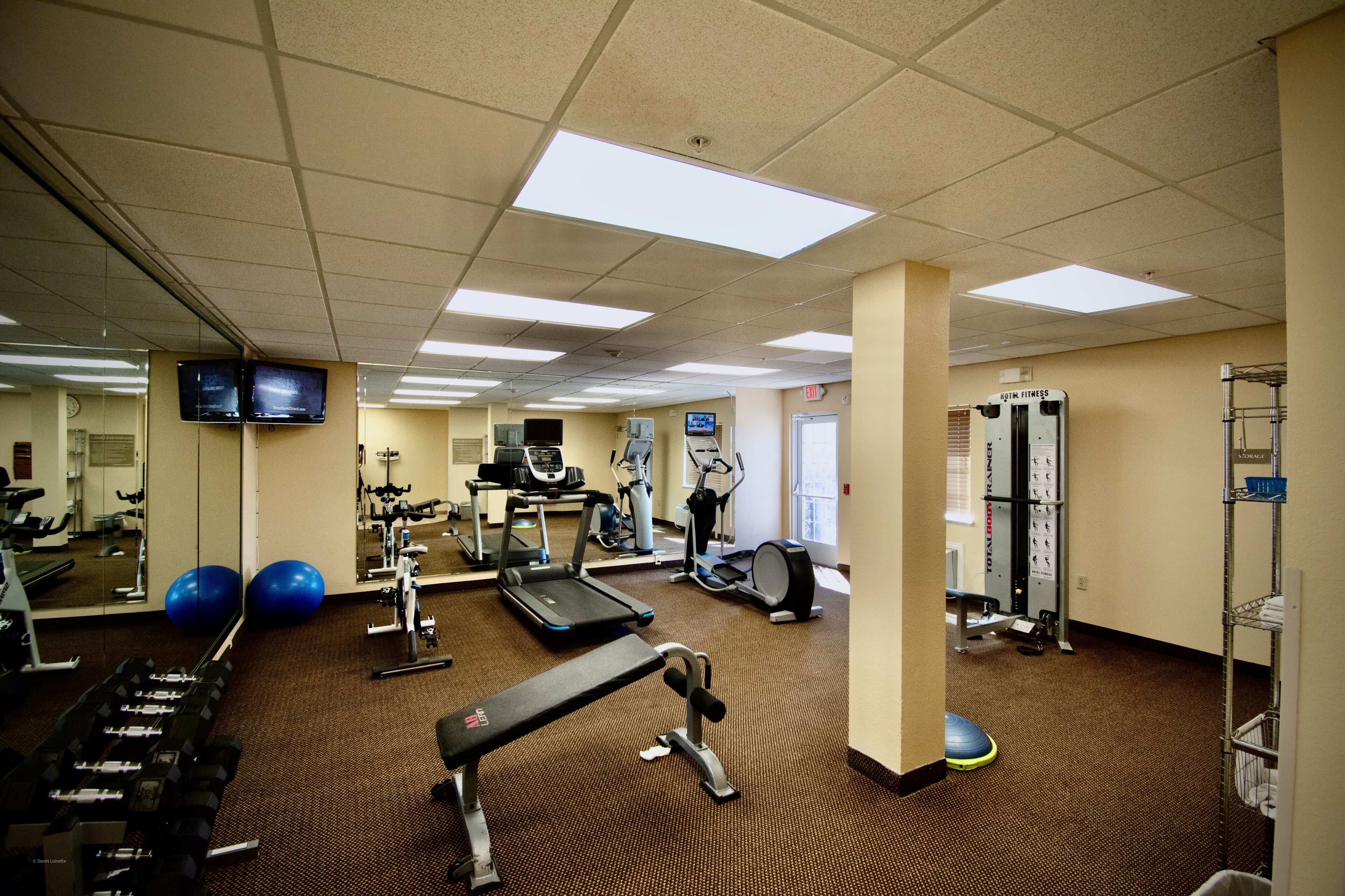 Une salle de sport équipée de machines d’exercice, d’un tapis de course et d’un mur recouvert de miroirs.
