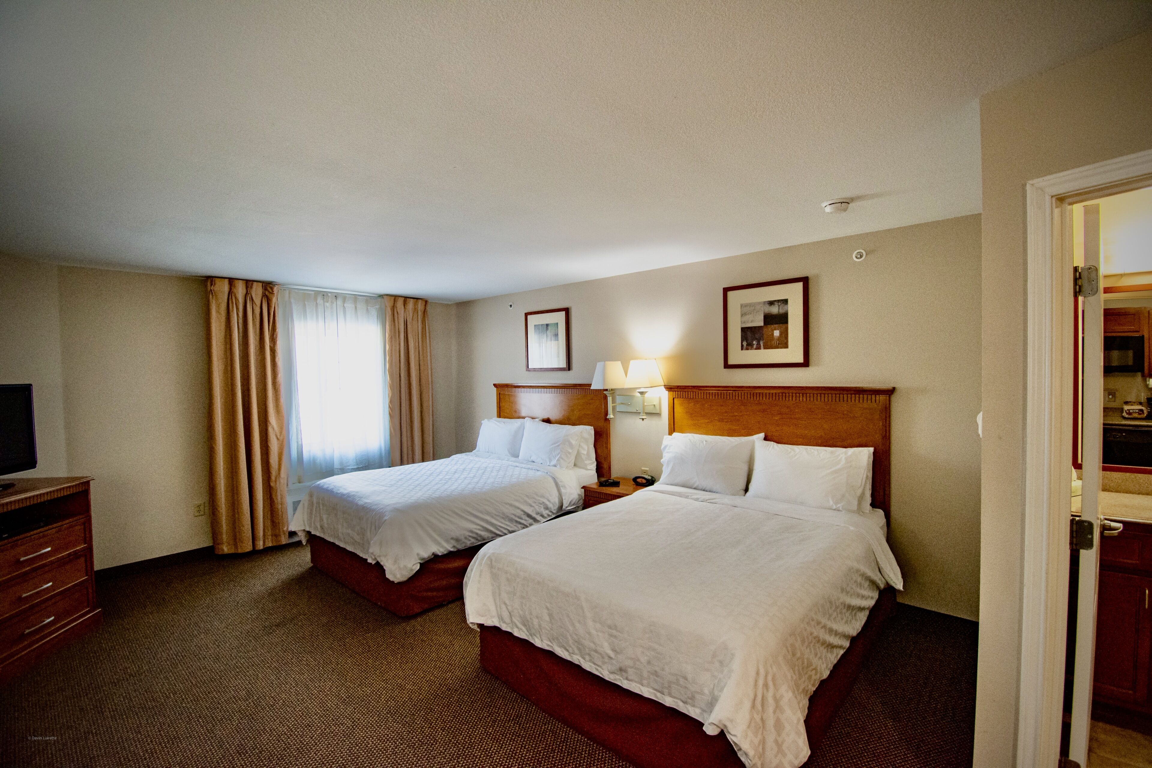 A hotel room with two beds, a television, a desk, and a window with curtains.