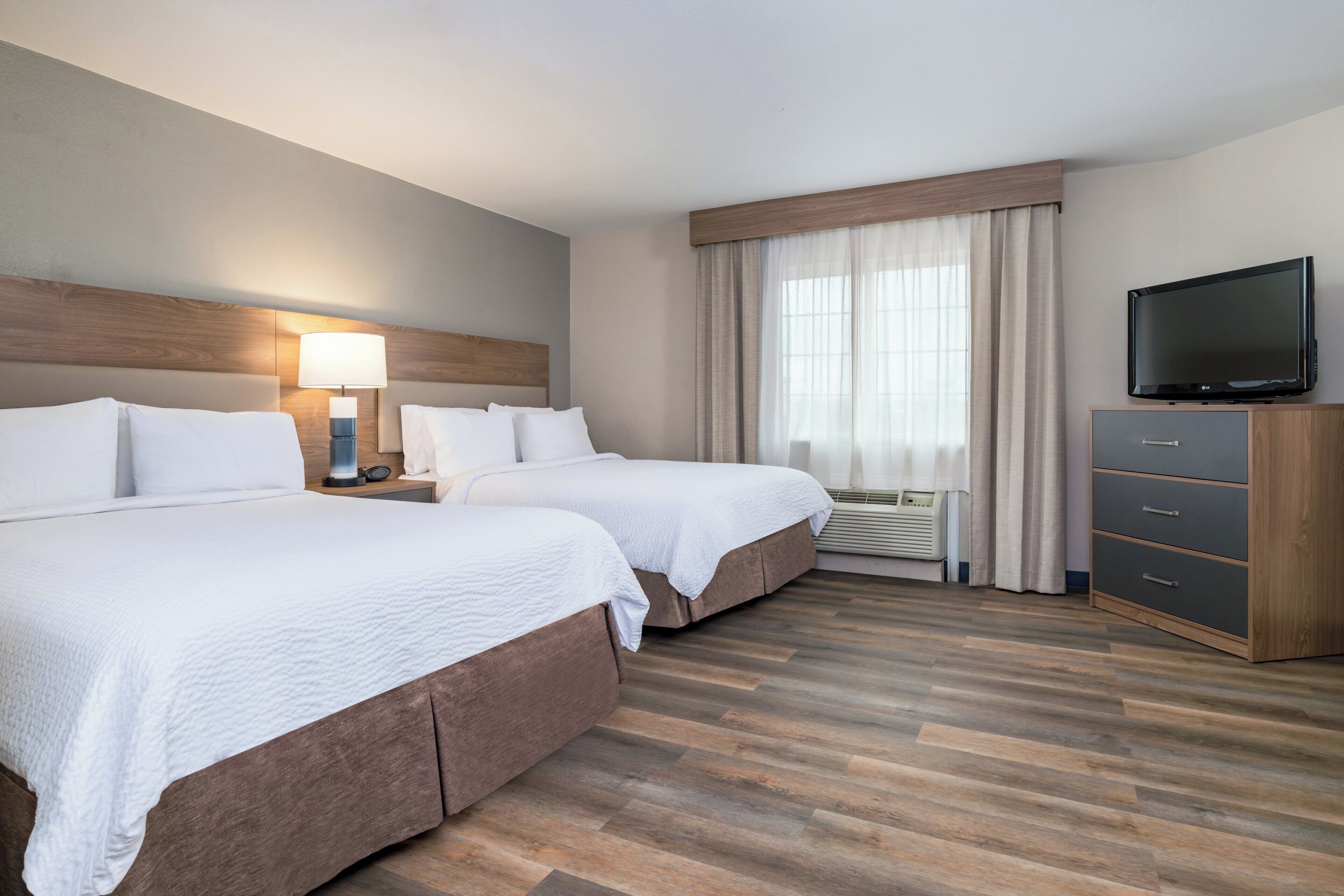 A hotel room with two beds, a TV, a lamp, and a wardrobe.
