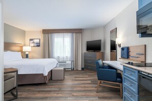 Ett hotellrum med en säng, ett skrivbord, en stol, en TV och ett litet pentry.