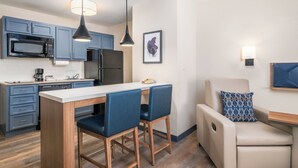 A modern kitchen with a microwave, stove, and dining area with chairs. - Candlewood Suites San Antonio NW Near Seaworld by IHG (San Antonio)