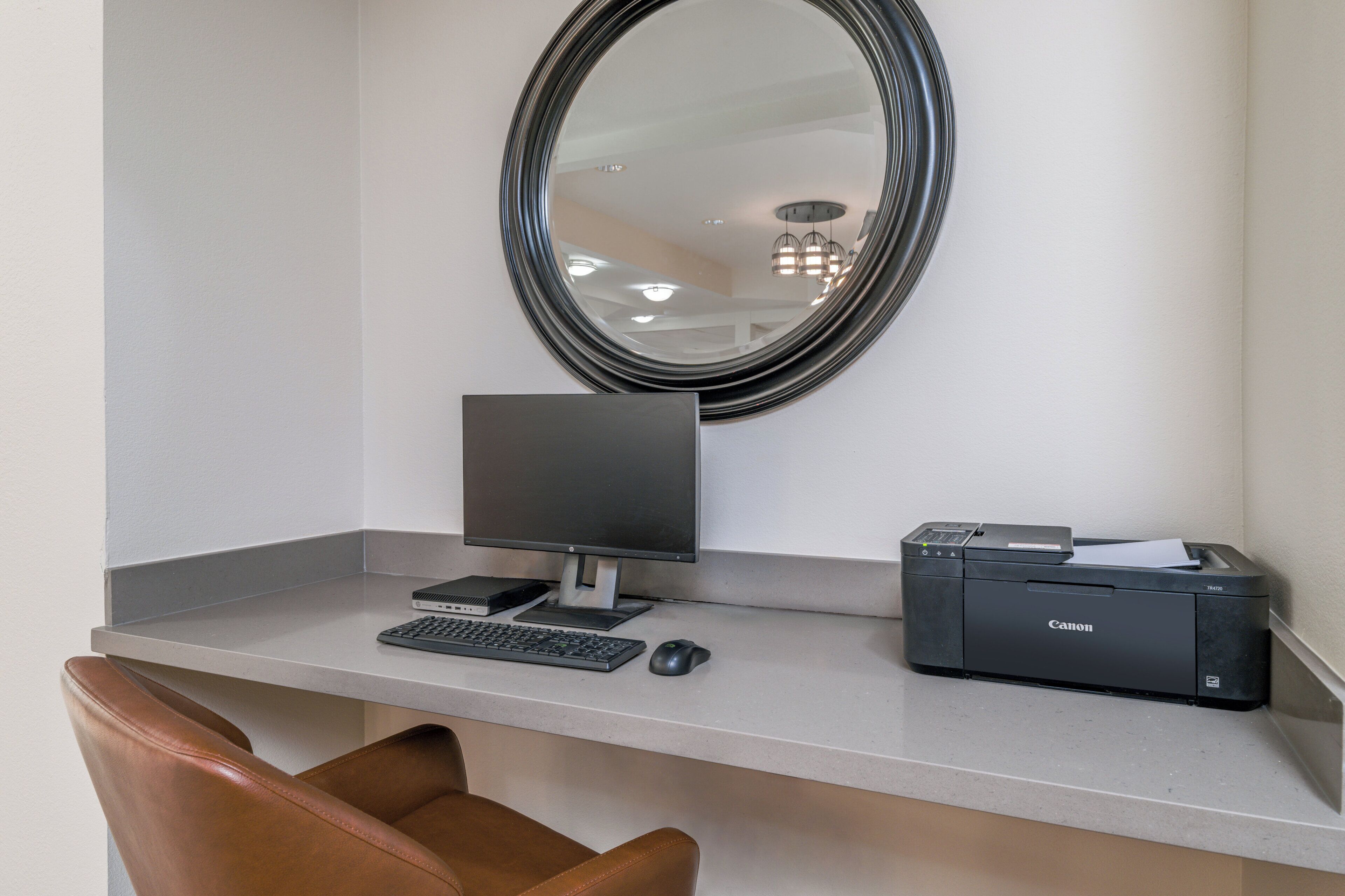 A workspace with a desk, a computer, a printer, a chair, and a mirror.