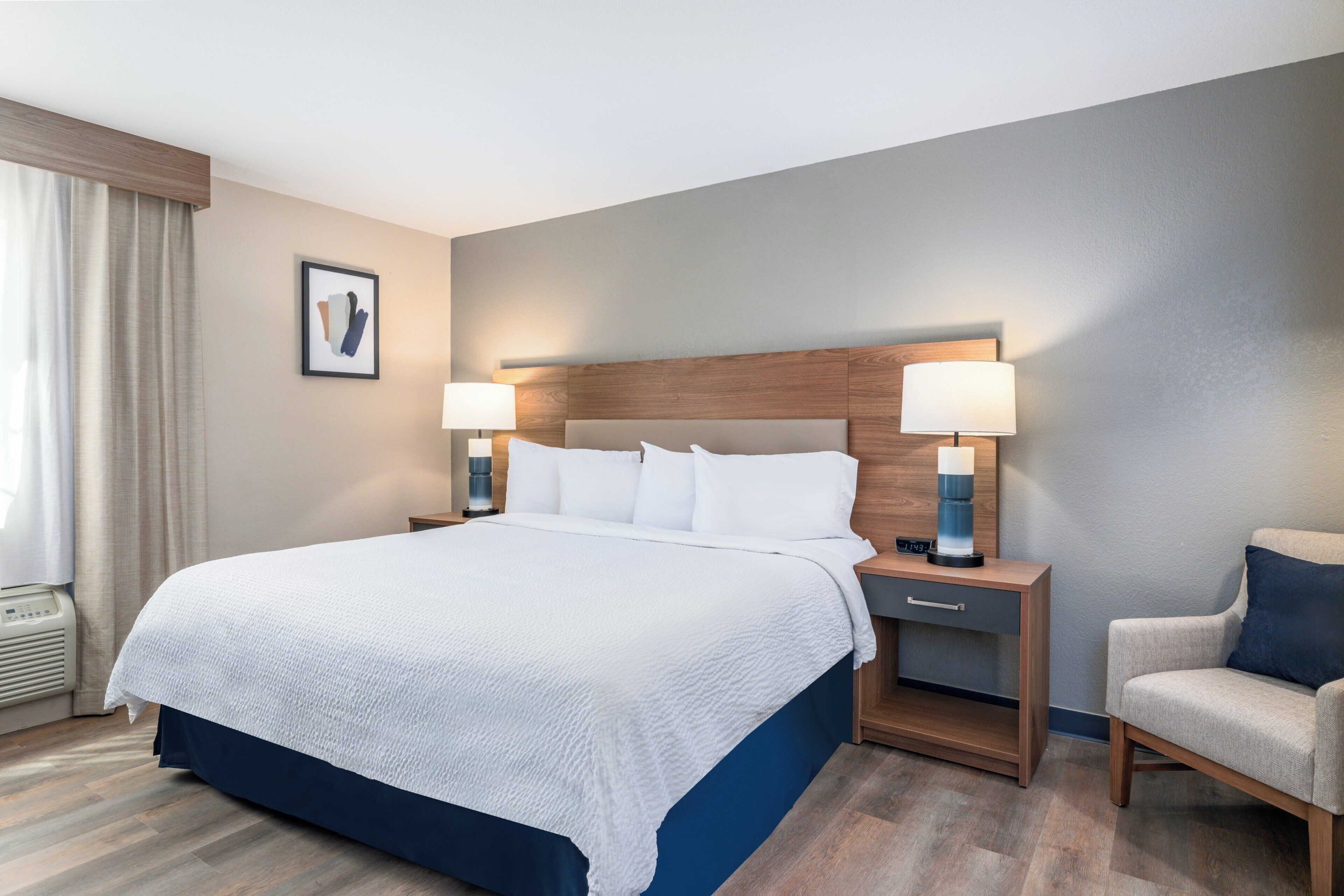 A hotel room with a large bed, two bedside tables with lamps, a chair, and a picture on the wall.