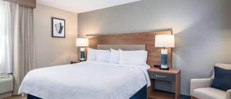 A hotel room with a large bed, two bedside tables with lamps, a chair, and a picture on the wall.