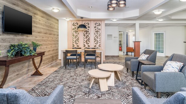 A modern lobby with a wooden wall, a flat-screen TV, a dining area with chairs, sofas, and a patterned rug. - Candlewood Suites San Antonio NW Near Seaworld by IHG (San Antonio)