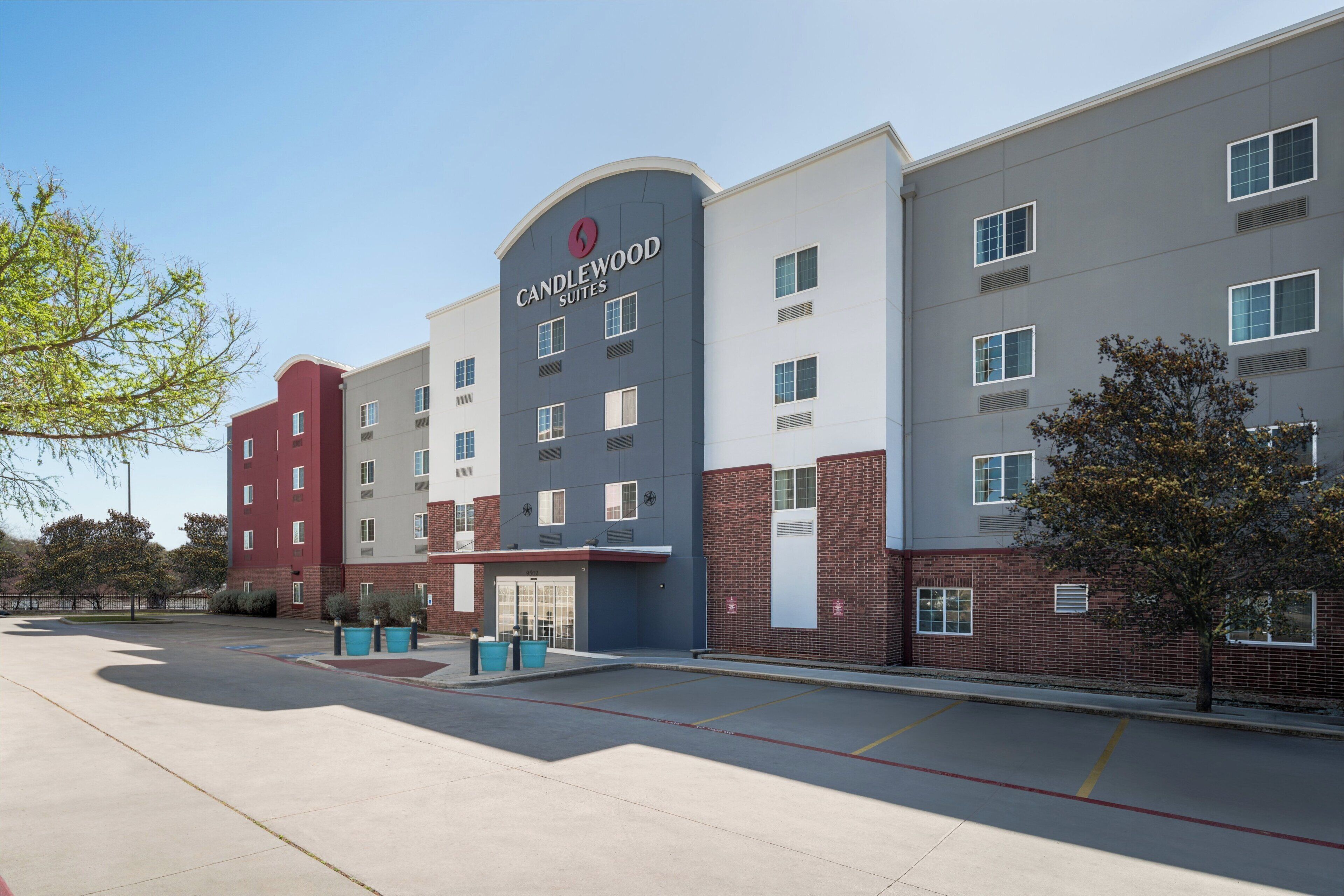 Un hotel de varios pisos con un llamativo letrero de 'Candlewood Suites', un estacionamiento y cielo despejado.
