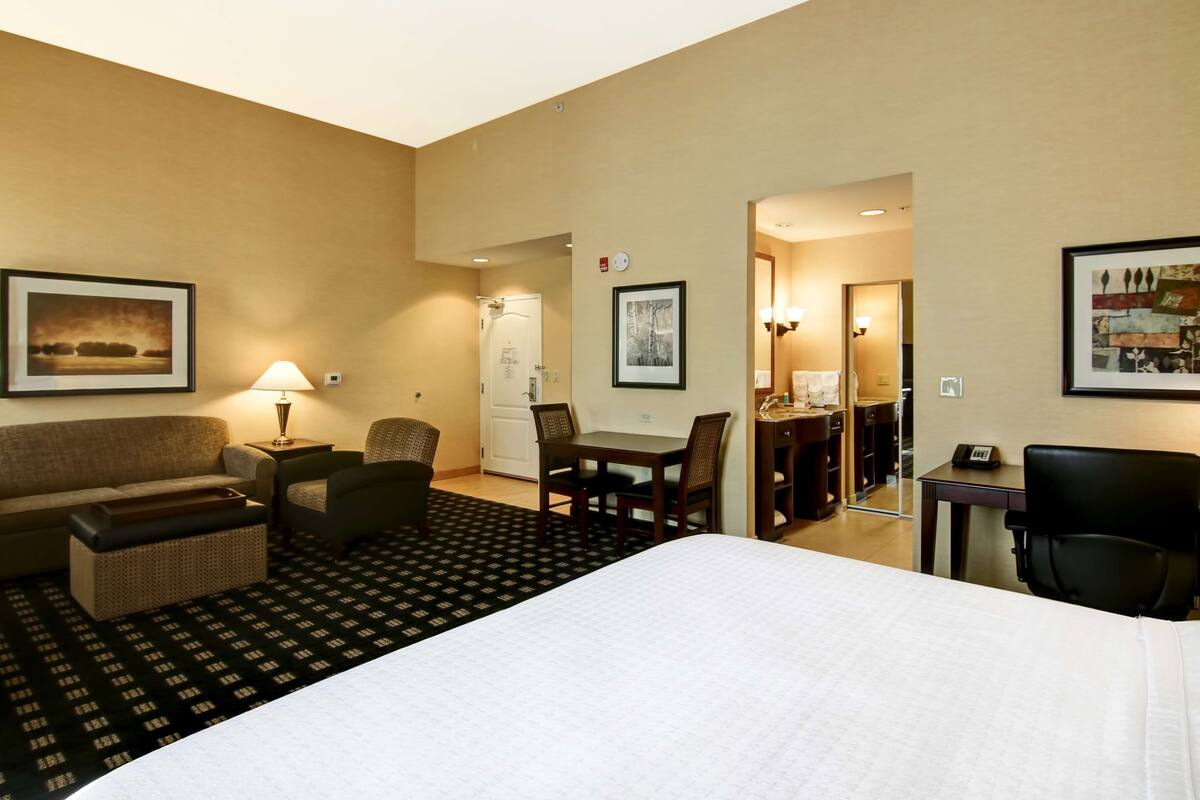 A hotel room with a bed, a desk, a chair, a sofa, and a dining table.