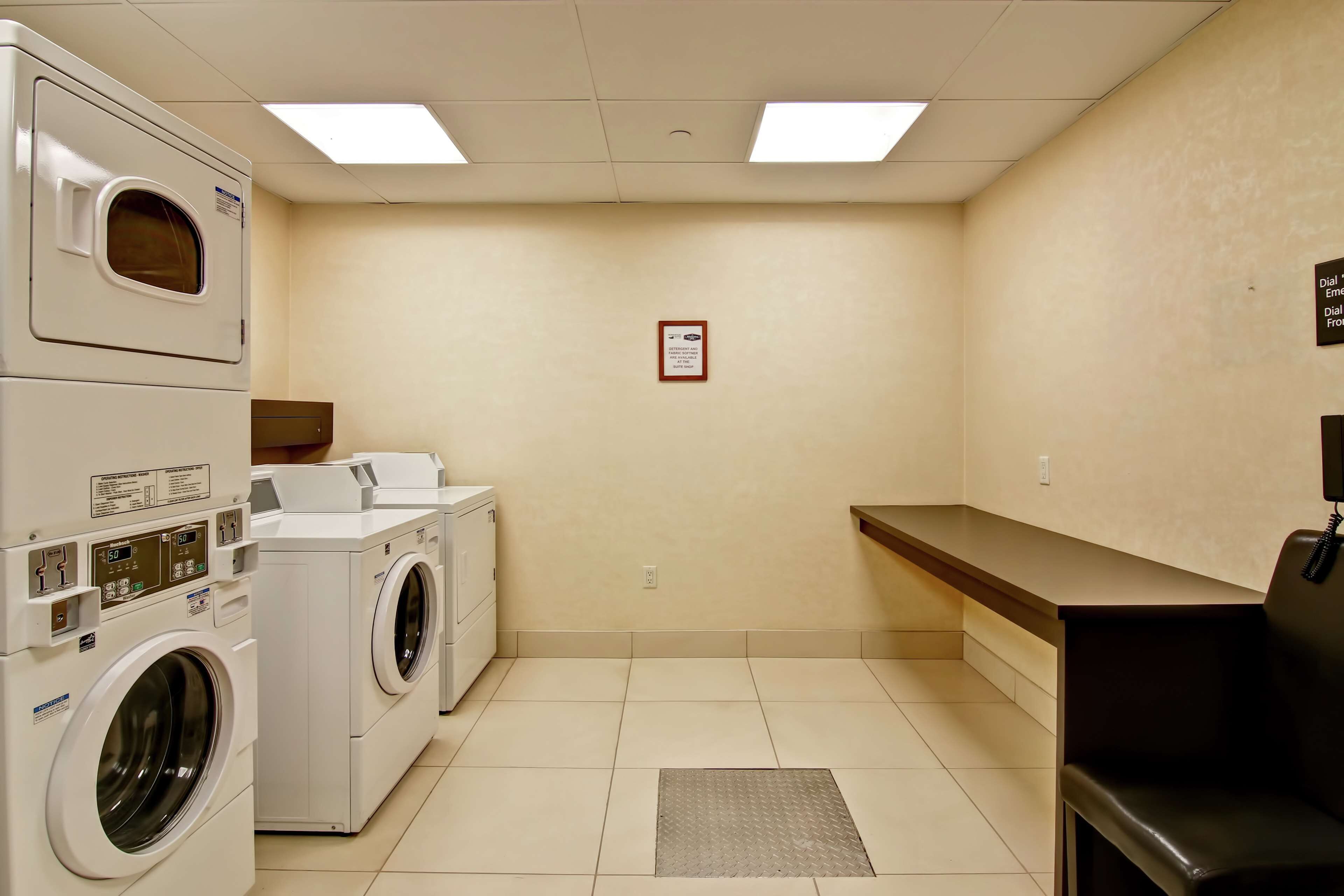 A laundry room with stacked washers and dryers, a bench, and a wall-mounted phone.