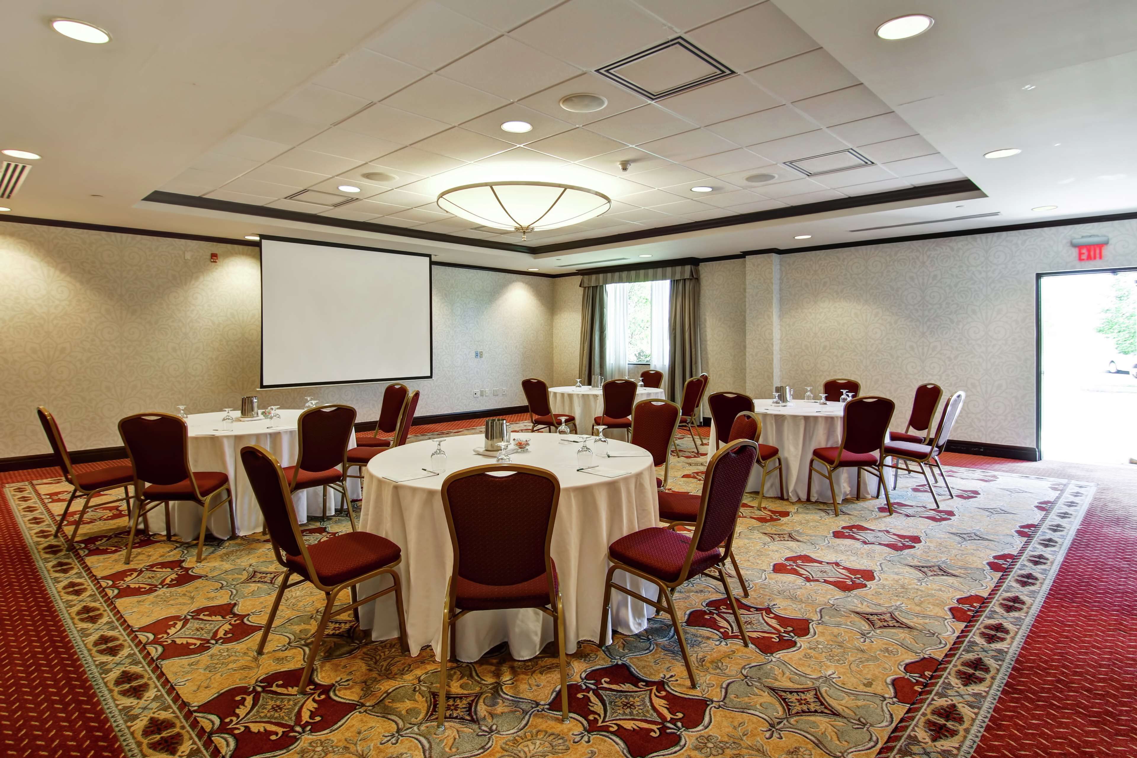 A conference room with round tables, red chairs, and a carpeted floor.