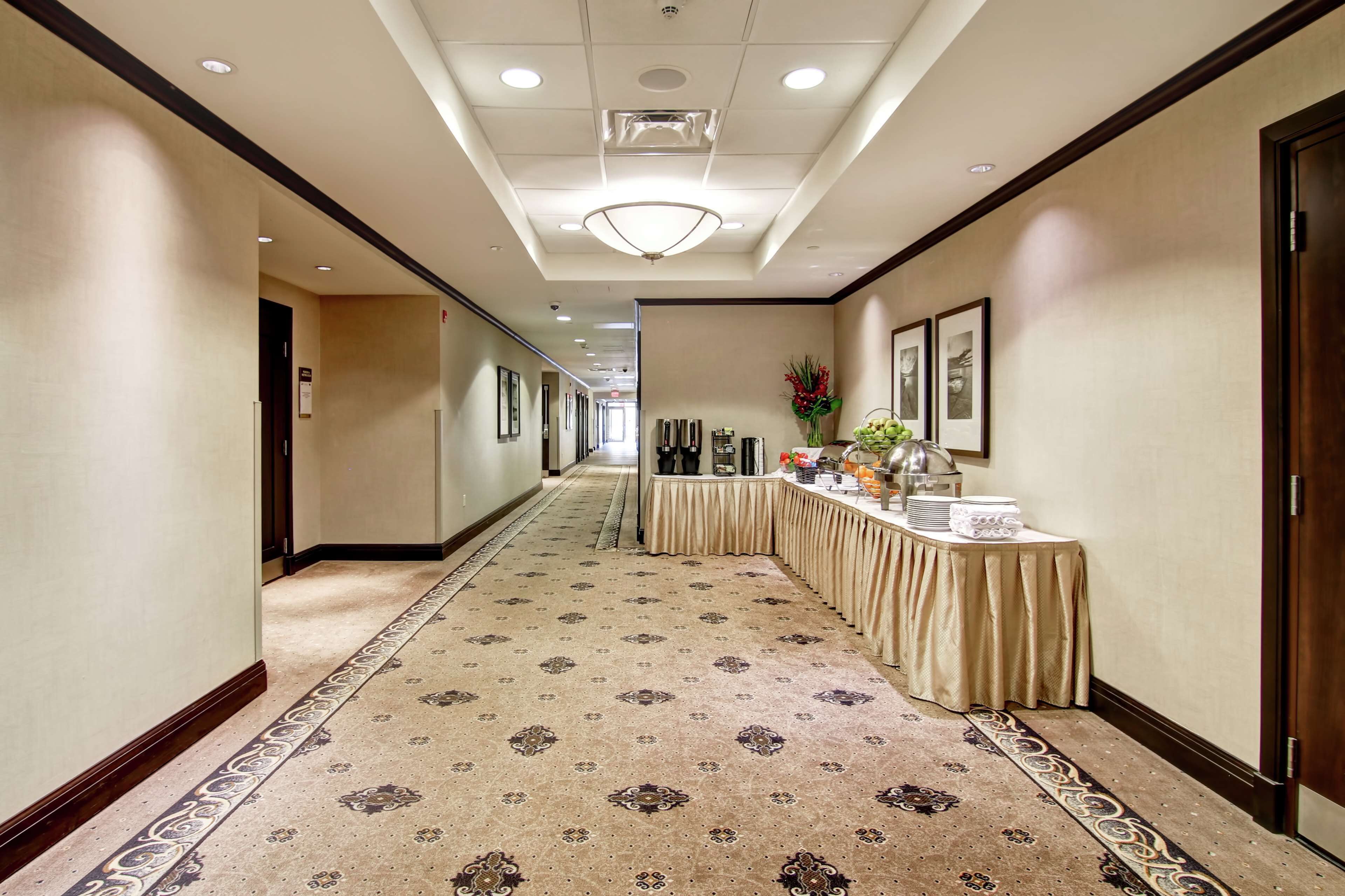 A hotel hallway with a patterned carpet, a reception desk with a table, framed pictures on the wall, and a chandelier.