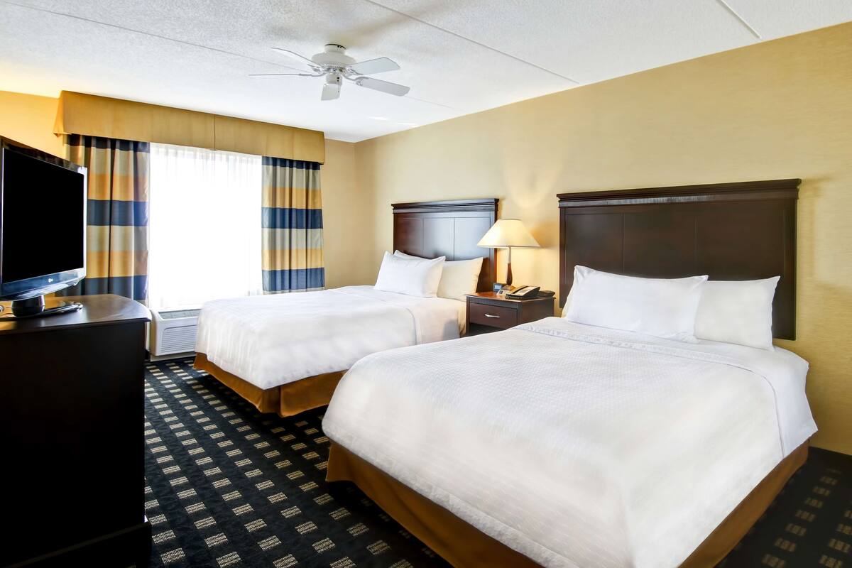 A hotel room with two beds, a TV, a ceiling fan, and a window with curtains.