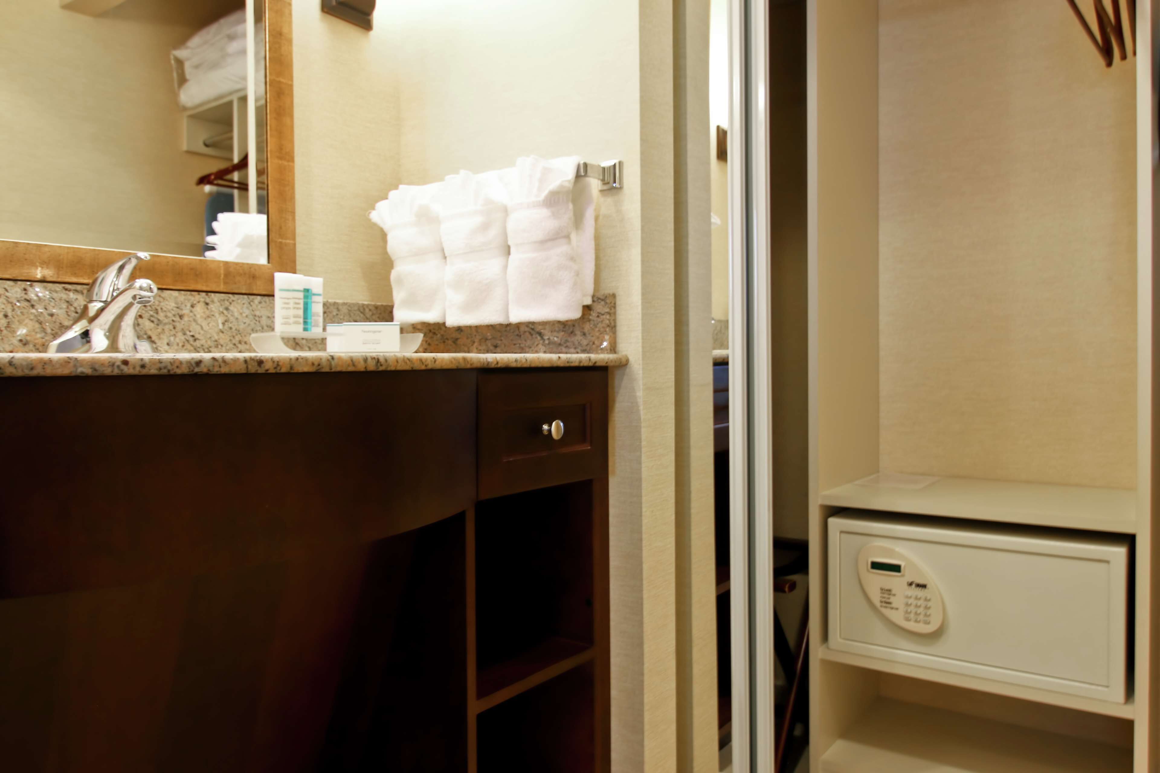 A bathroom with a granite countertop, a mirror, a towel rack, a small cabinet, and a safe.
