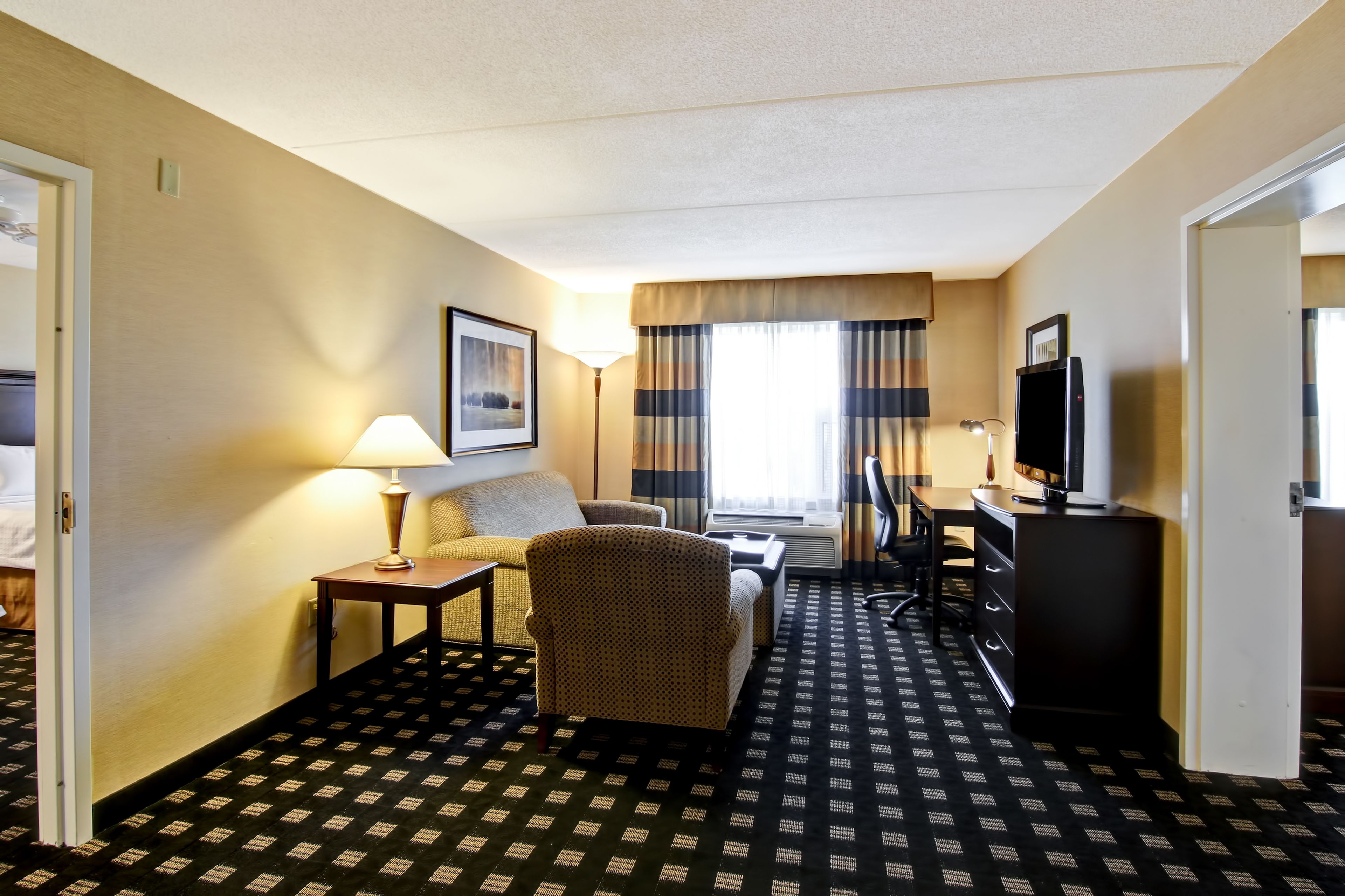 Habitación de hotel con sofá, sillón, escritorio y televisor.
