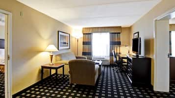 Habitación de hotel con sofá, sillón, escritorio y televisor.