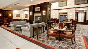 A hotel lobby with a fireplace, seating area, and a dining area. - Homewood Suites by Hilton Toronto Airport Corporate Centre (Toronto)