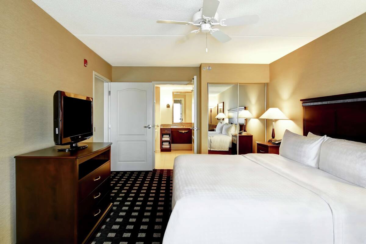 A hotel room with a bed, a television on a wooden dresser, a ceiling fan, and a bathroom visible through an open door.