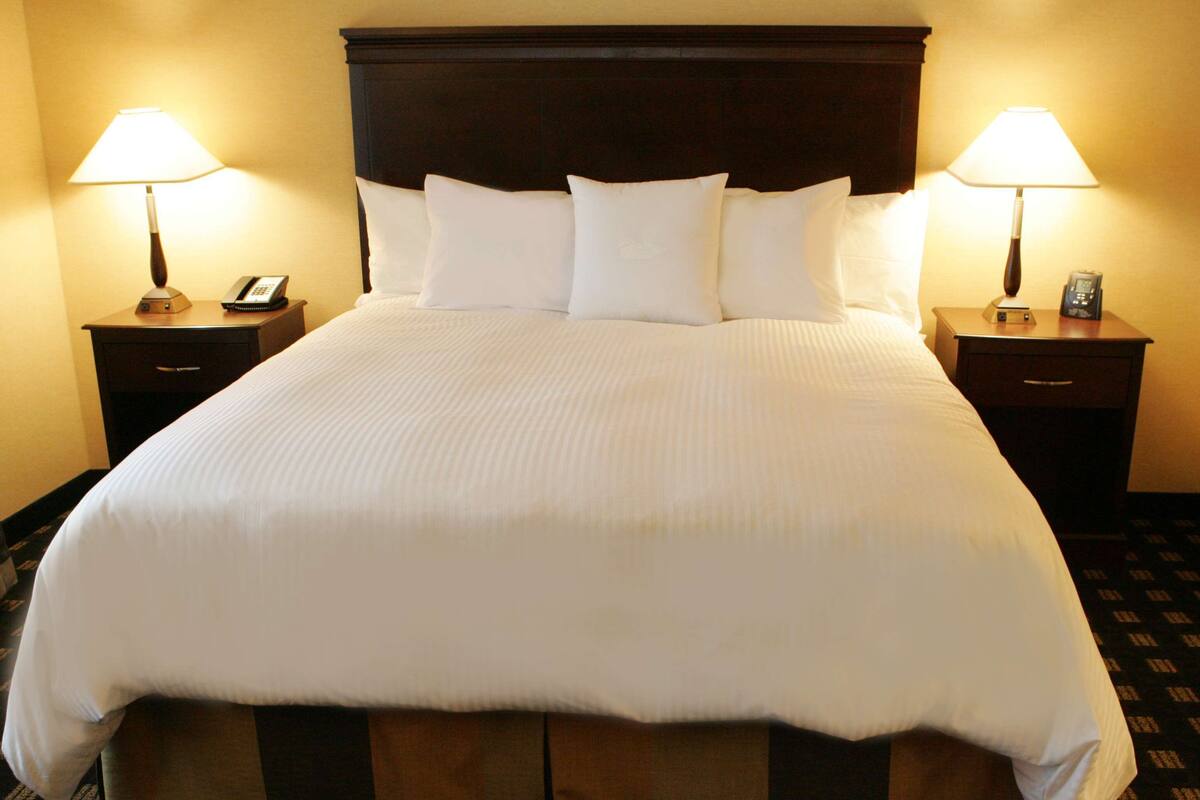 A large bed with white linens, flanked by two bedside tables with lamps and phones.