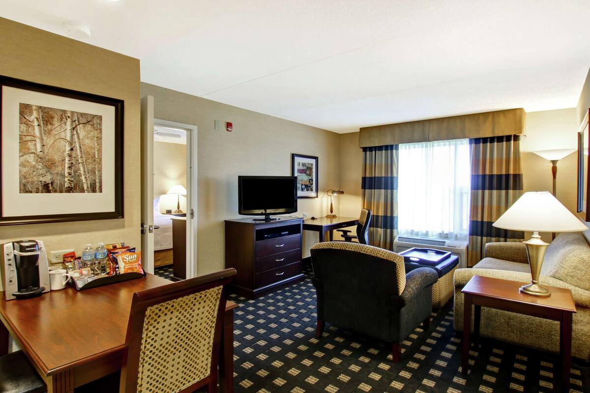 A hotel room with a bed, a desk with a computer, a television, a chair, a sofa, and a coffee maker.