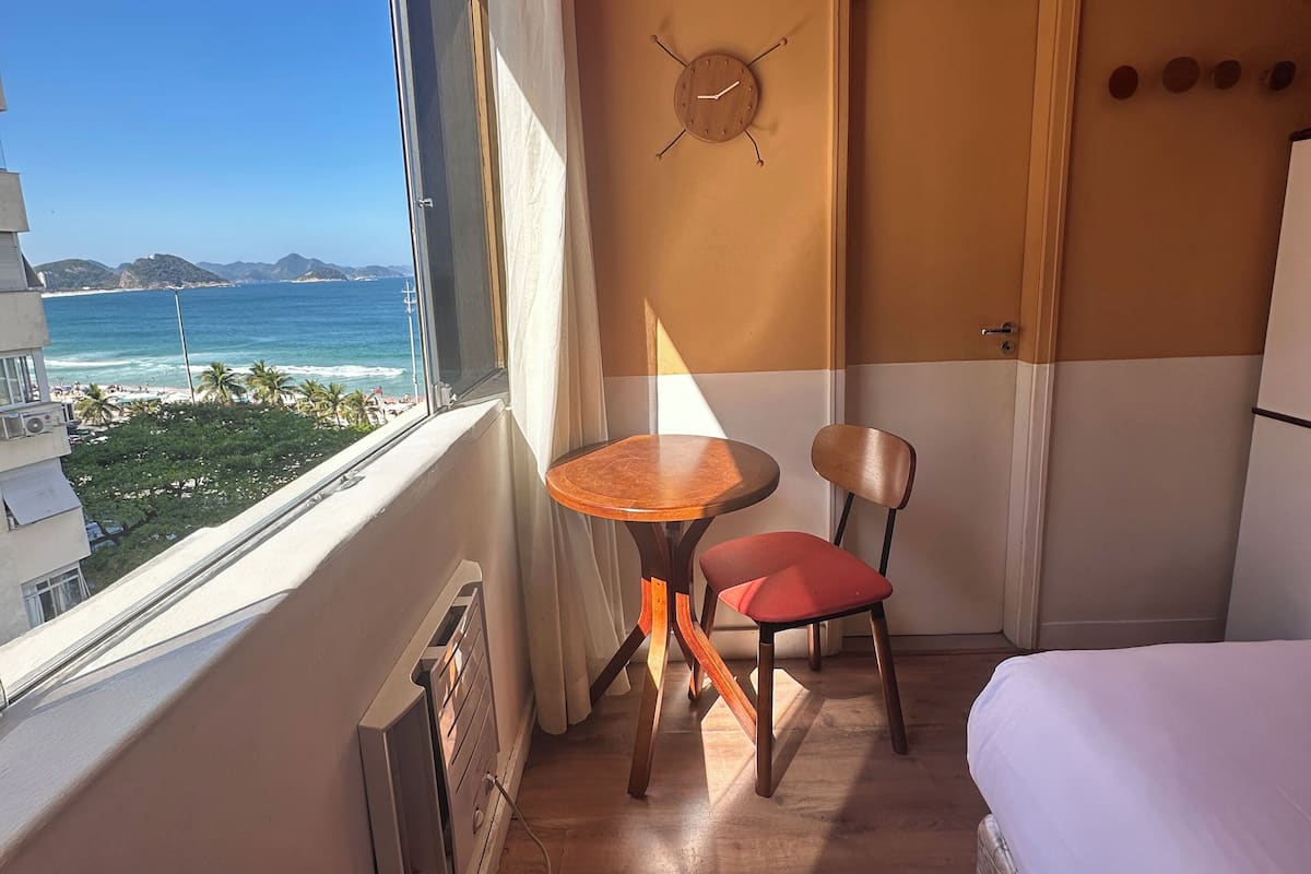 Habitación de hotel con cama, una mesa con silla, un reloj en la pared y vistas al océano.