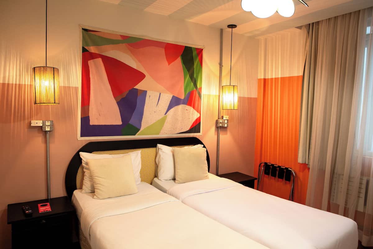 Habitación de hotel con una cama grande, dos mesitas de noche, un cuadro abstracto de colores y dos lámparas de pared.