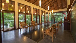 A spacious indoor area with wooden chairs and tables, large windows, and a high ceiling with exposed beams. - Tea Valley Resort (Devikolam)