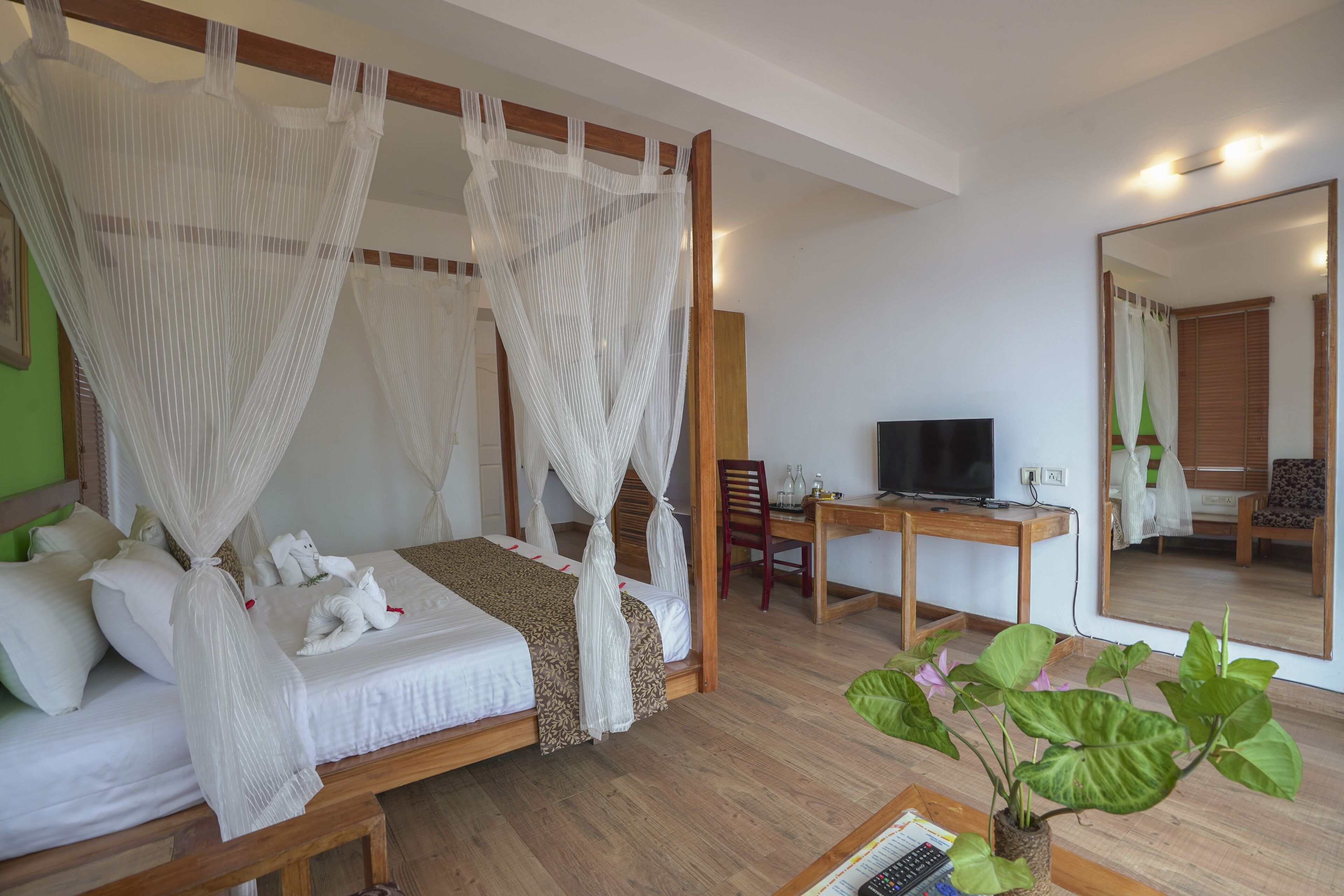 A four-poster bed with white linens, a wooden desk with a television, and a large mirror.