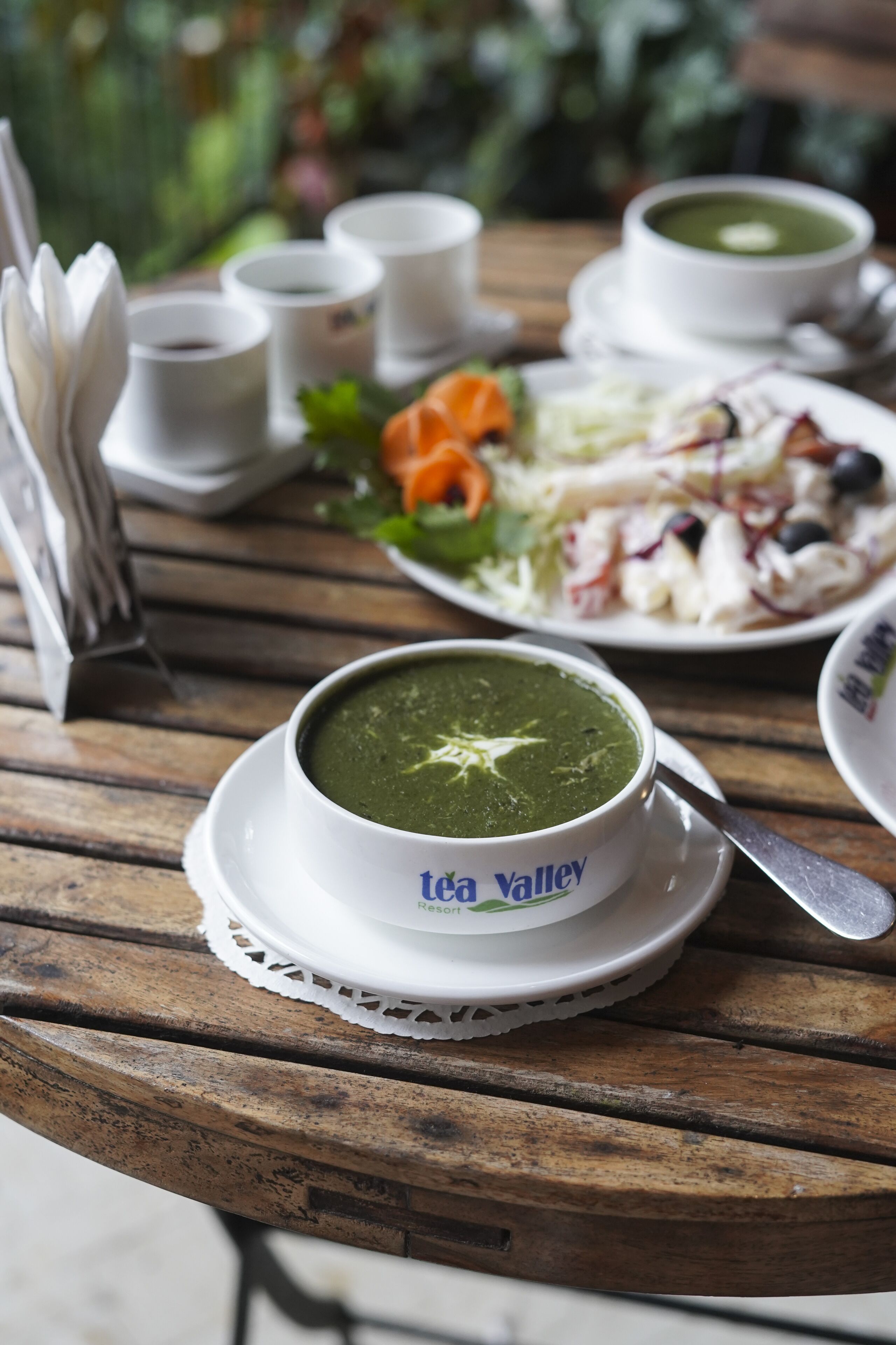 Un tavolo con una ciotola di zuppa verde, un piatto di cibo e diverse piccole tazze.