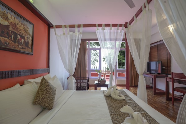 A hotel room with a bed, a television, and a balcony with curtains.