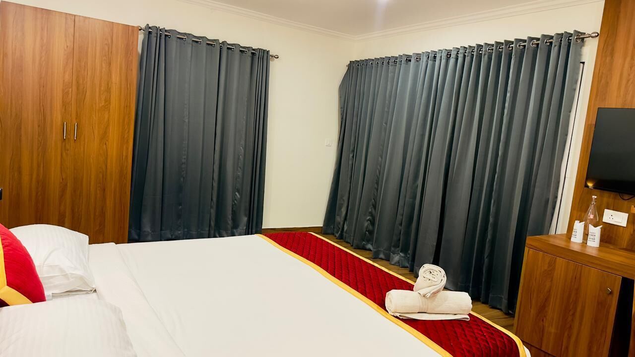 A hotel room with a bed, curtains, a wooden wardrobe, a television, and a red carpet.